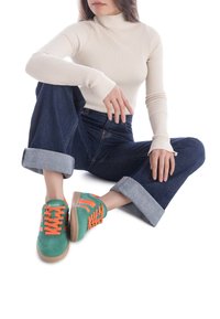 Baskets vertes et oranges en suède, avec une semelle en caoutchouc et des rayures contrastantes. Portées avec un jean en denim foncé retroussé et un col roulé côtelé.