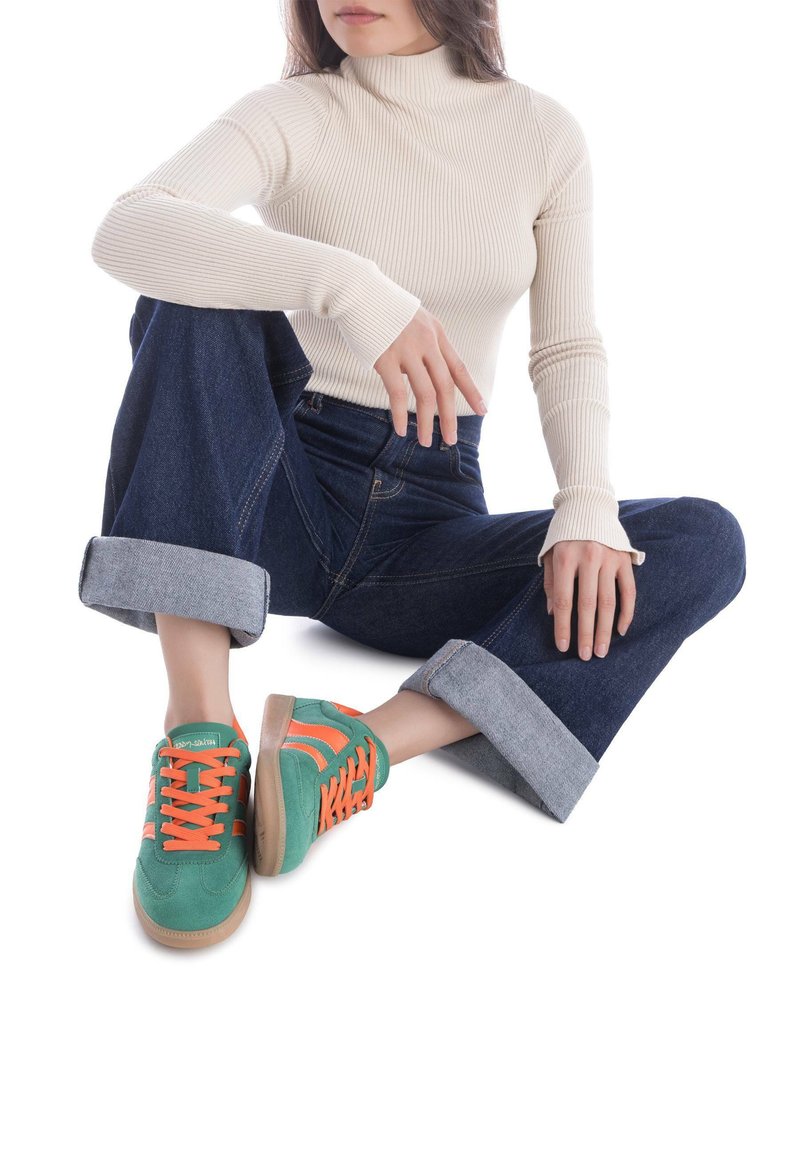 Baskets vertes et oranges en suède, avec une semelle en caoutchouc et des rayures contrastantes. Portées avec un jean en denim foncé retroussé et un col roulé côtelé.