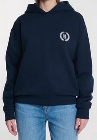 Sudadera con capucha azul marino hecha de mezcla de algodón, que cuenta con un bolsillo delantero tipo canguro, puños acanalados y un logo bordado dentro de un diseño de laurel.