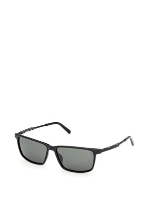 Schwarze, rechteckig gerahmte Sonnenbrille mit dunkelgrauen Gläsern, liegend auf einer weißen Oberfläche, im Winkel gezeigt, um Details der rechten Seite zu zeigen.