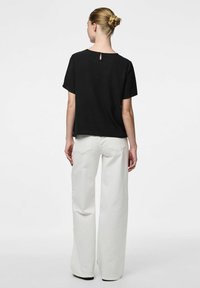 Top nero a maniche corte con dettaglio a chiave sulla schiena, abbinato a pantaloni bianchi a gamba larga in un tessuto semplice. Taglio semplice e rilassato con colori neutri.