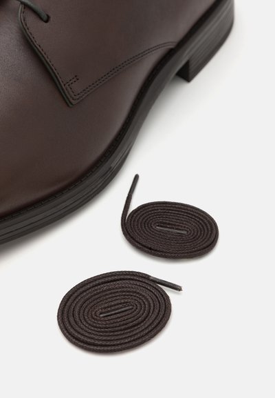 Chaussure en cuir marron avec une finition lisse, dotée de lacets ronds assortis et d'un bout arrondi, sur fond blanc.