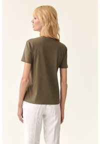 T-shirt verde oliva a maniche corte in morbido cotone. Collo rotondo classico, vestibilità rilassata, senza motivi visibili o dettagli in metallo.