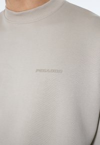 Beige sweatshirt med ribbet halsudskæring og struktureret stof. Har et præget "PEGADOR" logo på forsiden.