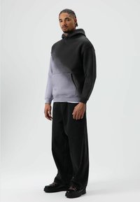 Capuchontrui met een verloop van zwart naar grijs, voorzien van een voorzak. Gecombineerd met loszittende zwarte denim broek en stevige zwarte schoenen.