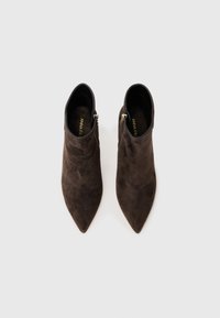 Botas de tobillo de ante marrón con diseño de punta afilada y cremallera lateral. La textura suave y la silueta ajustada ofrecen una apariencia elegante.