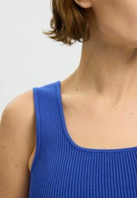 Ribbed bluza na ramiączkach z szerokimi szelkami, z dekoltem w serek i gładką teksturą, podkreślająca elastyczność i dopasowanie materiału.