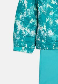 Giacca teal con un motivo testurizzato a macchie in bianco e verde chiaro. Presenta un tessuto liscio, una silhouette leggermente oversize e un orlo dritto.