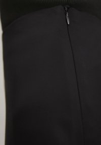 Vestido negro con textura de tela suave, cremallera oculta y un diseño estructurado con parte superior ajustada y sección inferior acampanada.