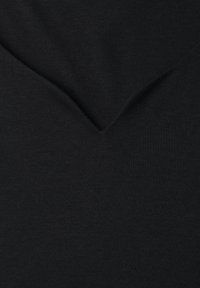 Gros plan sur un tissu noir avec un pli subtil en forme de V ou un détail de couture au centre.