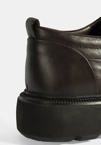 Chaussure en cuir marron à enfiler avec un bout arrondi et une épaisse semelle en caoutchouc noir. Présente une texture lisse et des détails de couture subtils.