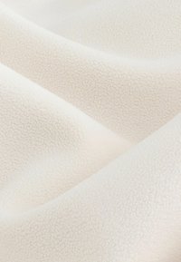 Weißer, texturierter Stoff mit einer sanften, flauschigen Oberfläche, die feine Falten und Knitter zeigt. Das Material wirkt leicht und glatt.