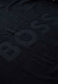 Asciugamano nero con la parola "BOSS" in grandi lettere in rilievo. Texture morbida con una finitura liscia, che mette in risalto un design minimalista.