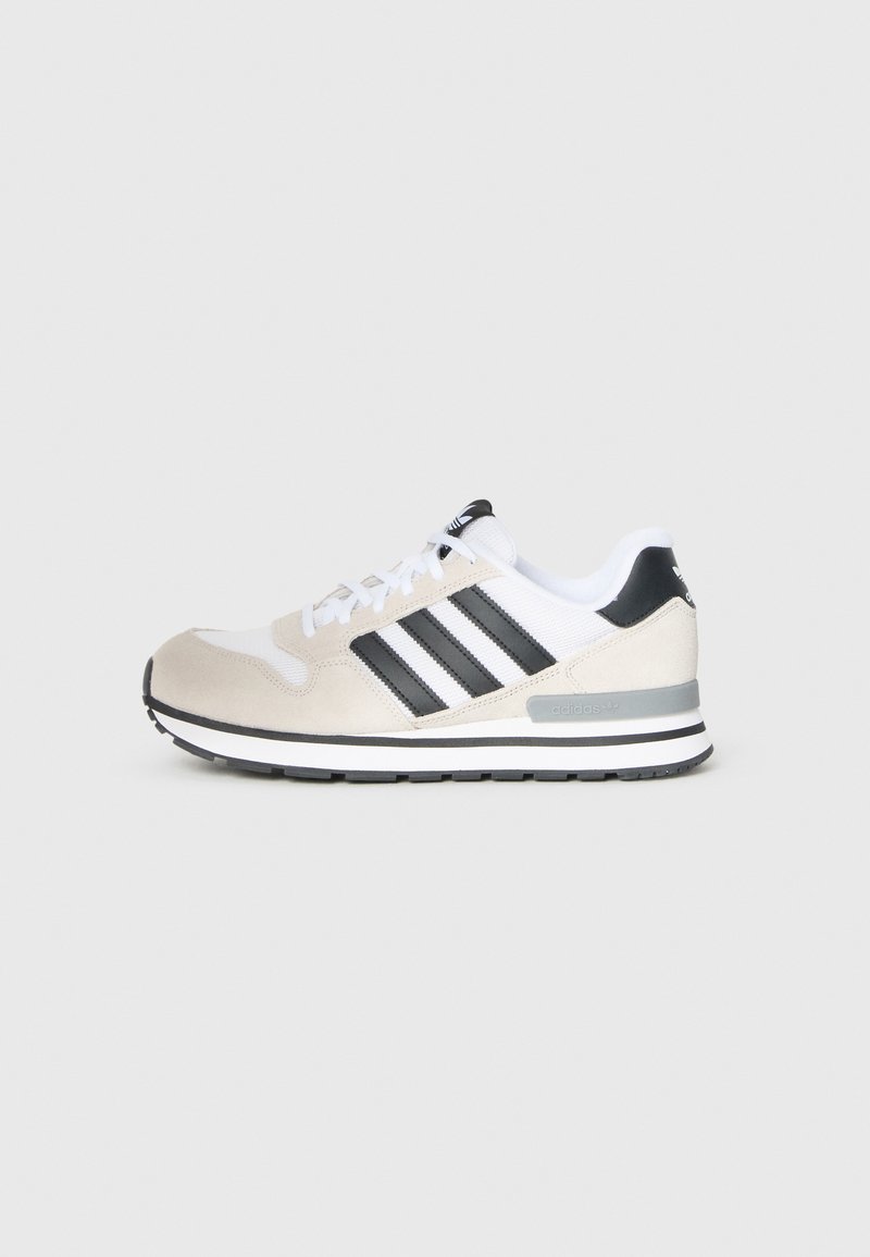 Bēša zamšādas un balta tīkliņa sneaker ar melnām svītrām, apaļu purngalu, baltām auklām, polsterētu apkakli un melnu papēža akcentu. Gumijas zole.