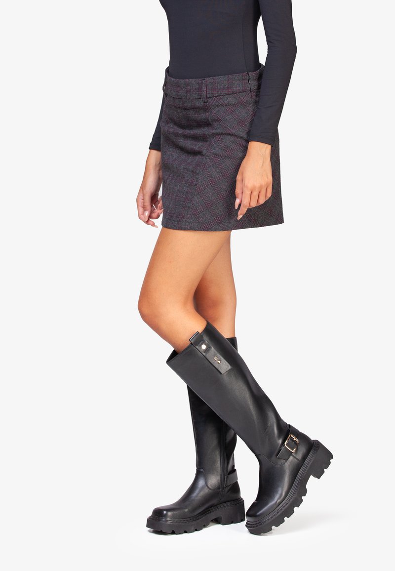 Jupe mini à carreaux dans des tons sombres avec une taille ajustée et des poches, associée à des bottes en cuir noir jusqu'aux genoux avec une semelle épaisse et des détails de boucle.