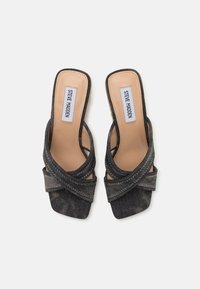Mules en denim à bout ouvert avec un design de lanières entrecroisées nouées. Couleur gris foncé avec un intérieur lisse et des détails de surpiqûres contrastants.
