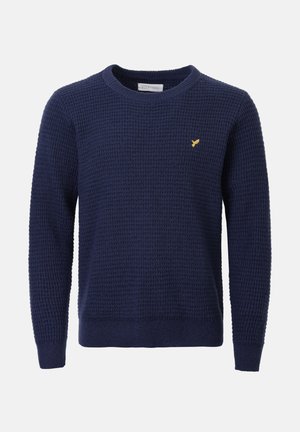 Jersey de punto azul marino con un patrón texturizado, cuello redondo y puños acanalados. Pequeño logo amarillo en el lado izquierdo del pecho.
