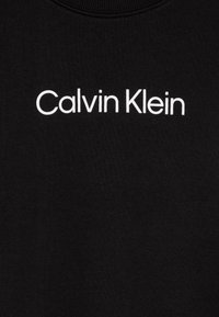Svart sweatshirt med en jämn textur, med vit text "Calvin Klein" centrerad på bröstet i ett modernt sans-serif typsnitt.