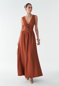 Maxi šaty v rustikálnej farbe s hlbokým V-výstrihom, nastaviteľným pásom, splývavou sukňou a textúrovanou tkaninou. Spárované so zdobenými svetlohnedými podpätkami.
