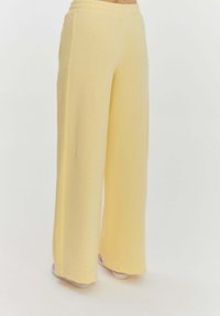 Žluté široké kalhoty s elastickým pasem, vyrobené z měkké tkaniny, s bočními kapsami a hladkým, netexturovaným povrchem.