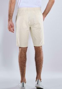 Beige linen shorts with an elastic waistband and side pockets, featuring a relaxed fit and hemmed edges, paired with white sneakers.