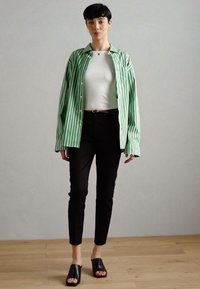 Zeleno-bílý pruhovaný shirt přes upnutý bílý top, doplněný černými kalhotami a černými pantoflí. Hladký materiál a volný střih.