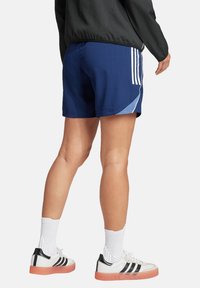 Marine sportieve shorts met lichtblauwe accenten en drie witte strepen. In combinatie met witte sneakers met zwarte strepen en een roze zool.