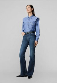Blaues Button-Up-Hemd mit zwei Brusttaschen, kombiniert mit dunkelblauen Schlagjeans und einem schwarzen Gürtel. Glattes Material mit taillierter Passform.