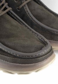 Scarpe in suede marrone scuro con suole in gomma beige, cuciture rinforzate e lacci rotondi. Il design include un accento testurizzato lungo il bordo.