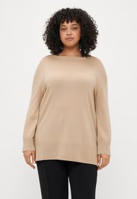 Μπεζ oversized πουλόβερ με στρογγυλή λαιμόκοψη, μακριά μανίκια, ριμπ μανσέτες και υφή πλέξης, συνδυασμένο με μαύρα παντελόνια.