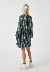 Robe à motifs floraux avec un design à étages, manches longues et encolure froncée. Panneaux multicolores sur un fond sombre.