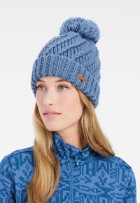 Blue knitted beanie with a textured pattern, featuring a fluffy pom-pom on top and a brown leather logo patch on the side.