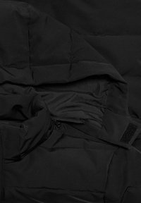 Black puffer jacket interior with quilted sections, featuring a zipper pocket and a Velcro strip. Smooth nylon fabric texture.