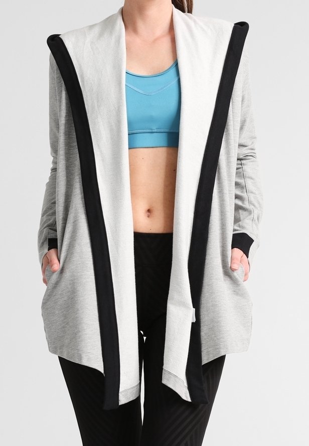 Cárdigan ligero de color gris con ribetes negros, diseño de abertura frontal, mangas largas y bolsillos laterales, perfecto para llevar sobre ropa deportiva.