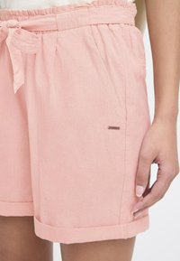 Lyse rosa shorts laget av pustende stoff, med elastisk midjebånd og knyttet belte. Har sidelommer og rullet kantdetalj.
