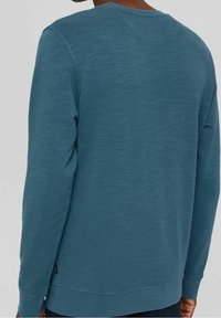 Sudadera azul con cuello redondo, mangas largas y un acabado texturizado. Incluye detalles de costura sutiles y una etiqueta en el dobladillo.
