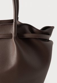 Καφέ δερμάτινη τσάντα tote με υφή, που διαθέτει δύο λαβές και απαλό, μαζεμένο άνοιγμα. Ο σχεδιασμός είναι μινιμαλιστικός και λειτουργικός.