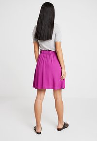 Fuchsia skaterkjol med en samlad midja, tillverkad av lättviktig tyg, i kombination med en grå t-shirt och svarta slidesandaler.