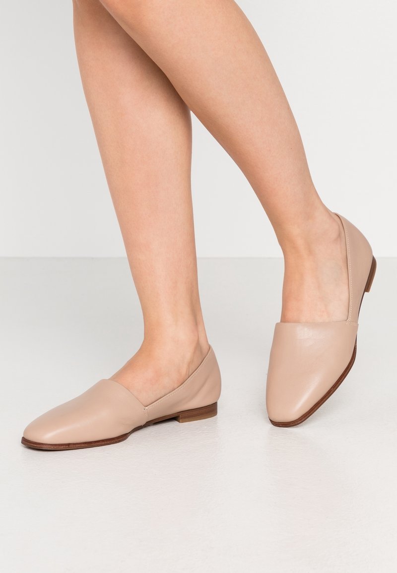 Chaussures à enfiler en cuir nude, à bout pointu et talon carré bas, présentant une texture lisse et un design minimal.