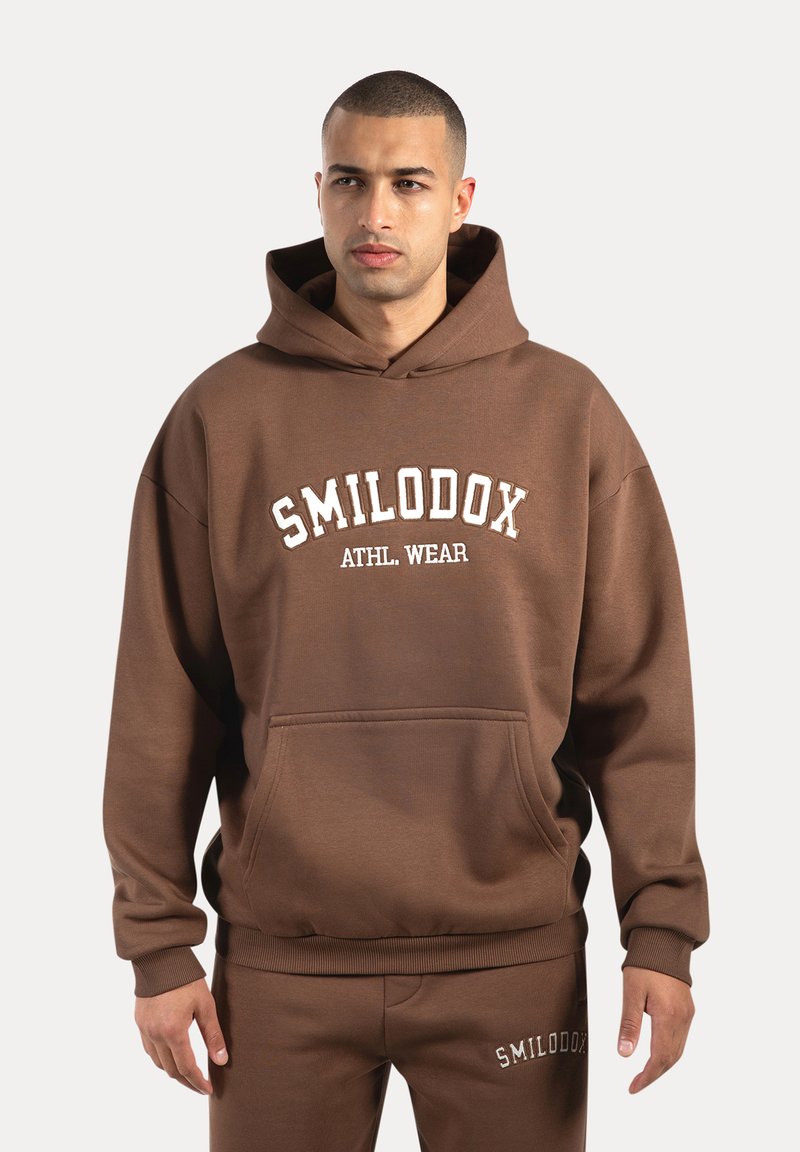 Sweat-shirt à capuche marron en tissu doux, doté d'une poche frontale, de poignets côtelés et de l'inscription "SMILODOX ATHL. WEAR" sur la poitrine.