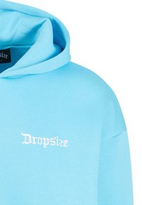 Helle blaue Kapuzenjacke aus weichem Material mit einer großen Fronttasche. Verfügt über eine Kordelzugkapuze und ein gesticktes "Dropsize"-Logo in Weiß.