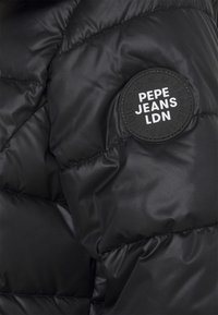 Czarna pikowana kurtka puchowa z przeszyciami, z okrągłą czarną naszywką z napisem "PEPE JEANS LDN." Gładka, matowa faktura.