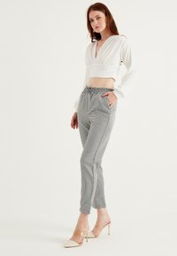 Top bianco cropped a maniche lunghe con scollatura a V profonda abbinato a pantaloni grigi a righe tapered con vita elastica e tasche laterali.