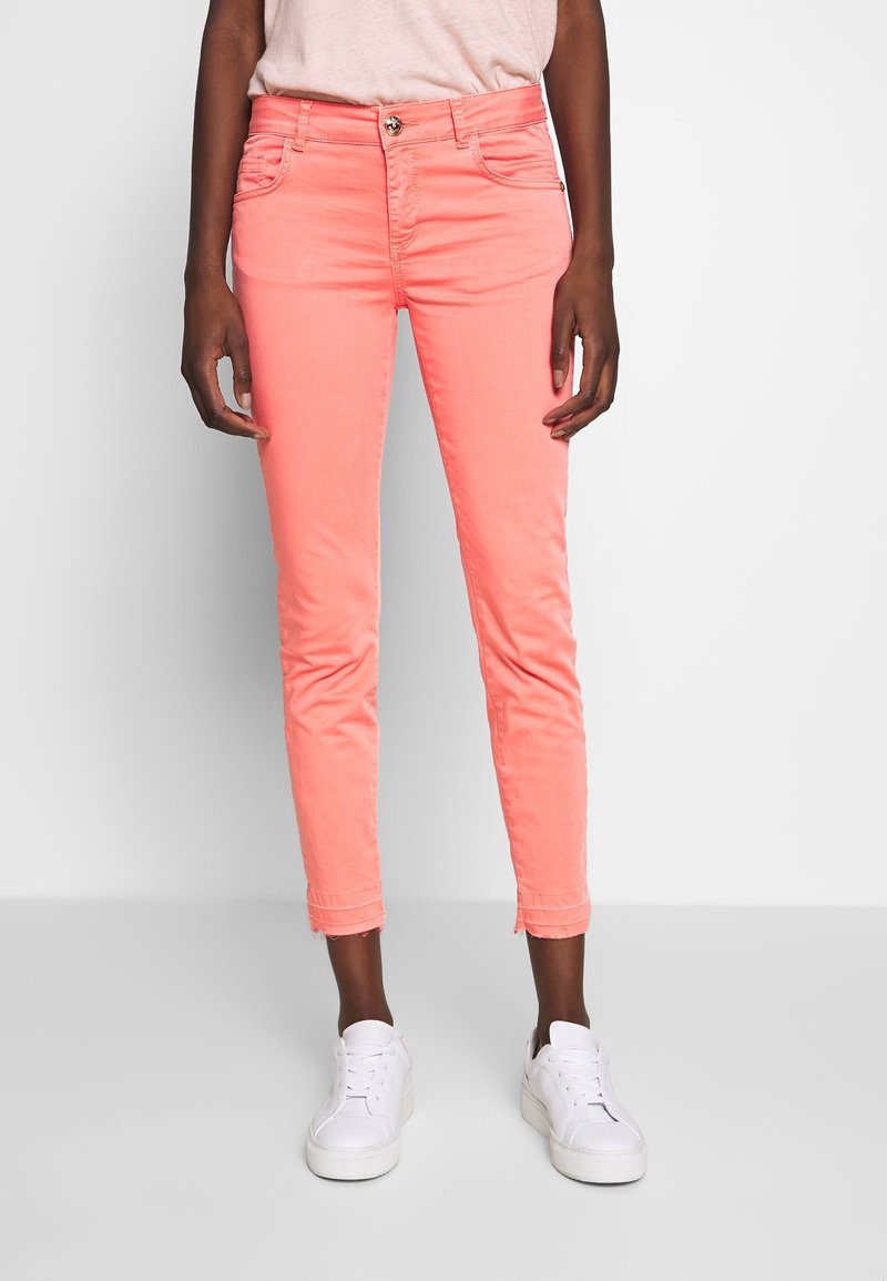 Jean skinny en coton rose avec taille mi-haute, cinq poches et ourlet surpiqué. Associé à des baskets blanches.