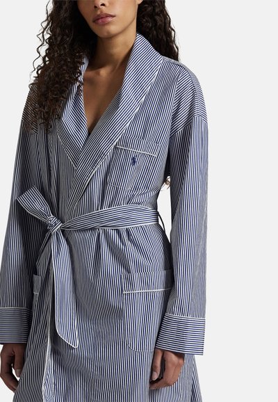 Ριγέ ρόμπα σε ναυτικό μπλε και λευκό, κατασκευασμένη από απαλό ύφασμα. Διαθέτει γιακά σάλι, ζώνη στη μέση, μακριά μανίκια και τσέπες με αντίθετο περίγραμμα.