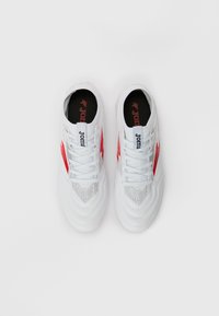 Pantofi sport albi cu un design texturat, având accente roșii și o talpă interioară neagră pe care este afișat în mod proeminent numele brandului "Joma".