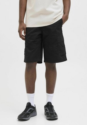 Pantaloni cargo neri con più tasche, taglio fino al ginocchio e una texture di cotone liscia. Abbinati a scarpe da tennis nere e calze bianche.