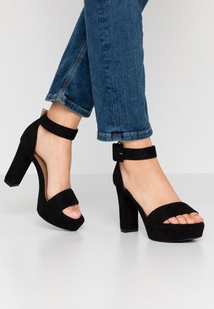 Zwarte suede hoge hak sandalen met dikke blokhakken, enkelbandjes en een open teen ontwerp; gladde textuur en minimalistische stijl.