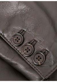 Dunkles Ledergewebe mit drei runden Knöpfen mit vier Löchern, die durch eine Naht am Rand gesichert sind. Glatte Textur mit einem subtilen Glanz.