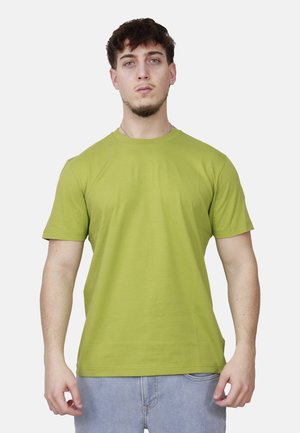 Giovane uomo che indossa una maglietta a maniche corte verde lime e jeans azzurri chiari su uno sfondo chiaro e uniforme.